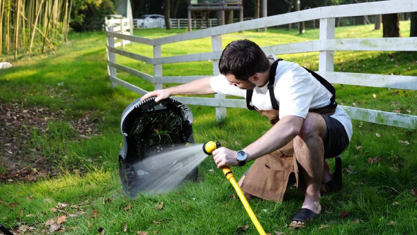 Person using a garden hose to water a lawn in a grassy area with a white fence in the background. washing down a N2000 Novabot Lawn Mower
