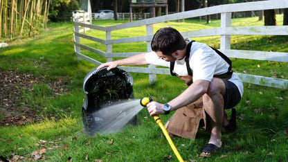 Person using a garden hose to water a lawn in a grassy area with a white fence in the background. washing down a N2000 Novabot Lawn Mower